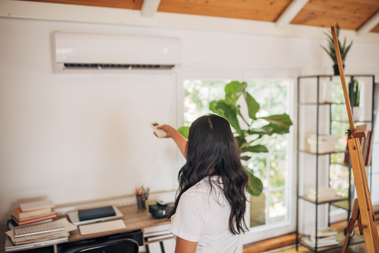 woman in home office using remote control to turn on air conditioner mounted on wall