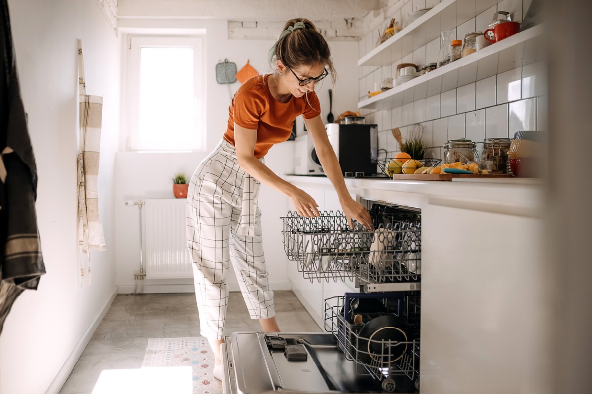 woman in striped pants loading her dishwasher in narrow kitchen