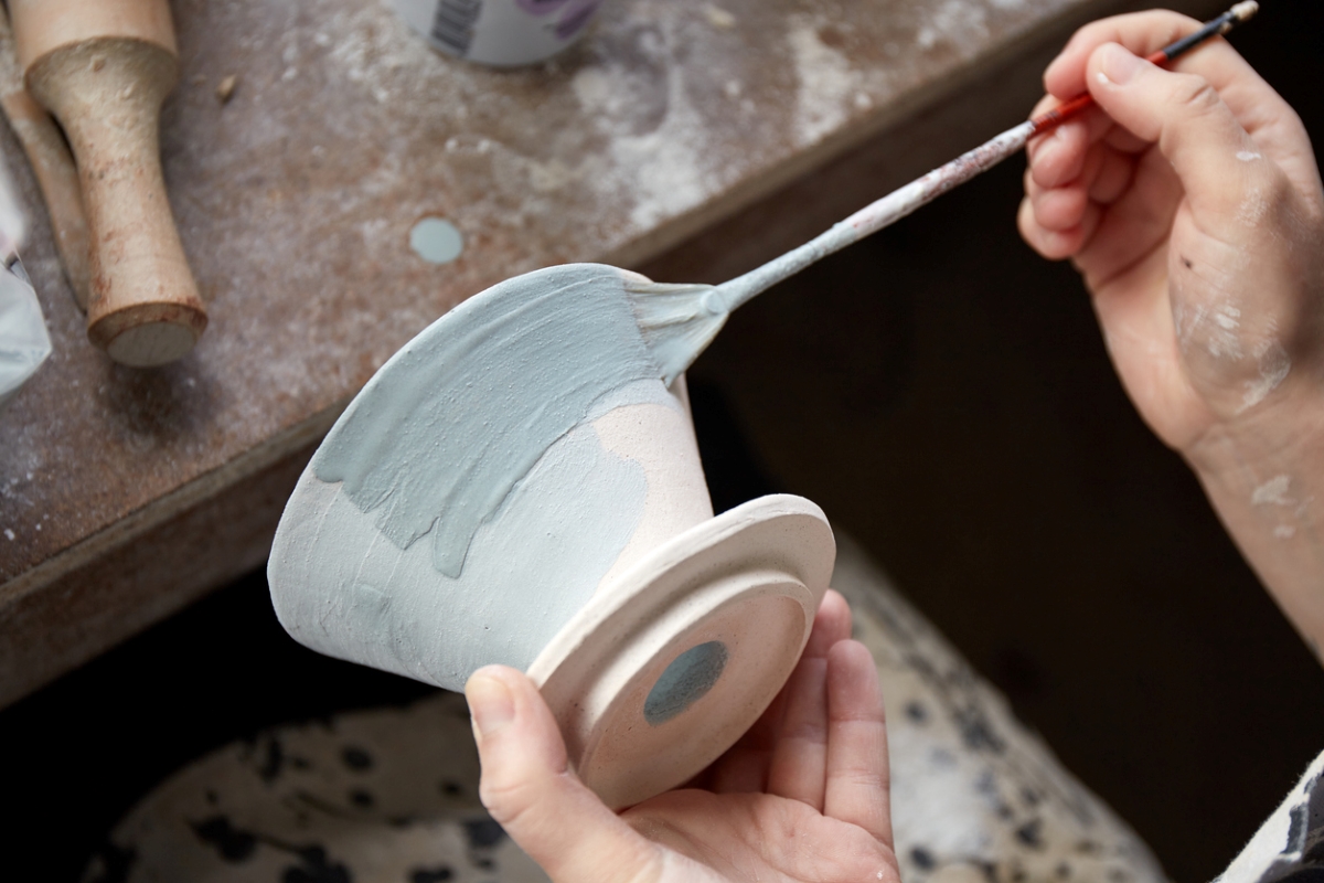 person brushing on pottery glaze