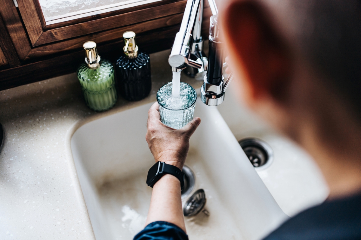 person filling glass cup from faucet