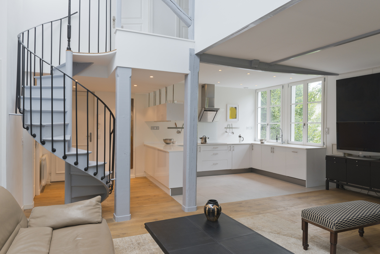 Wide angle of living space and kitchen with spiral staircase.