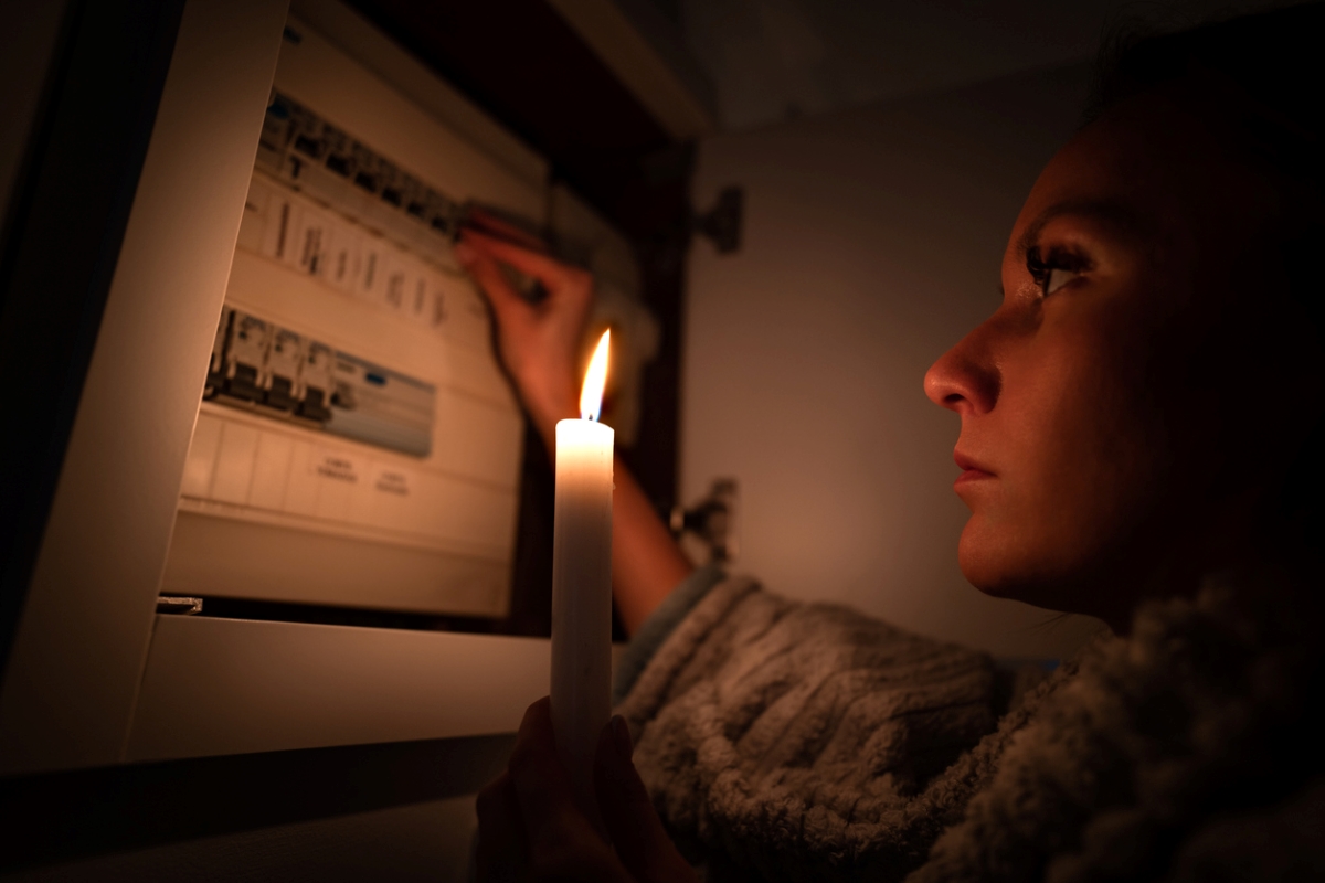 Woman checking fuse box while holding lit candle