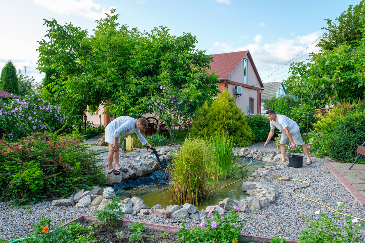 two-men-do-maintenance-on-a-backyard-pond-surrounded-by-greenery