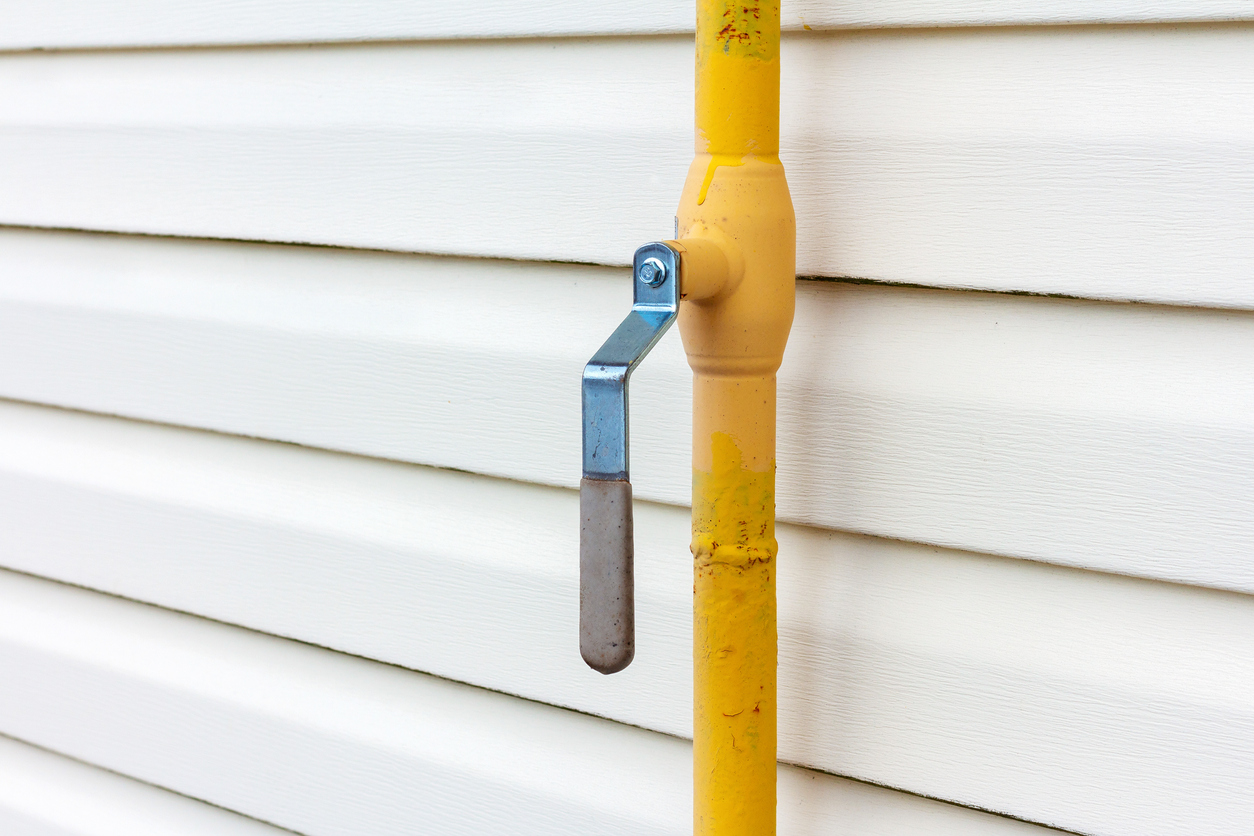 Yellow gas pipe with manual valve on the wall of the house