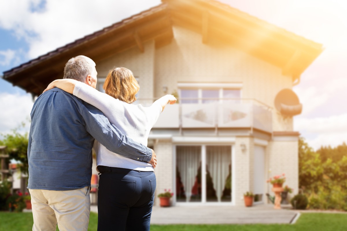 Rear View Of Senior Couple Pointing Finger In Front Of House