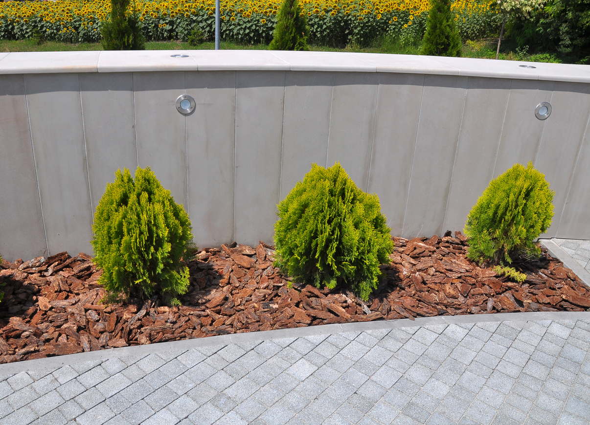 Brick chip planter bed with green shrubs planted in it, surrounded by gray brick path.