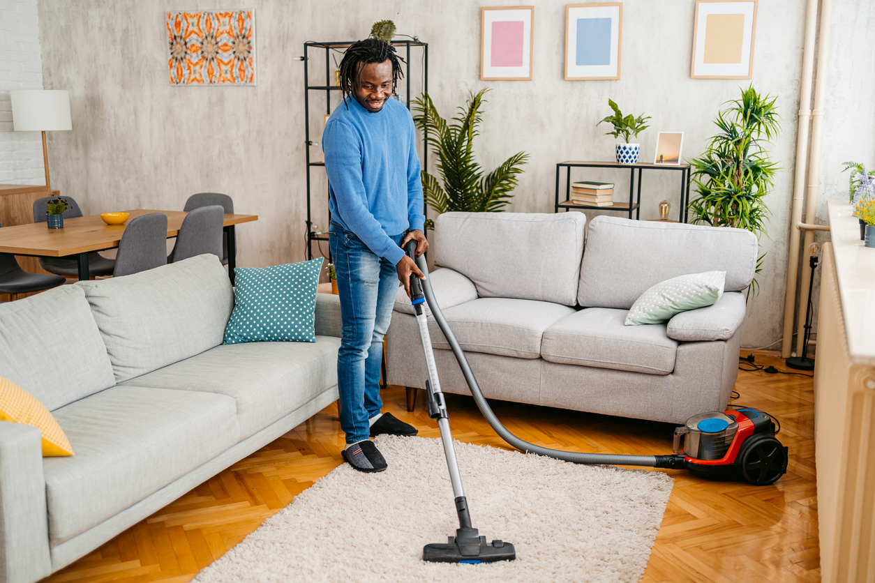 Handsome young black man vacuuming the carpet in his apartment.