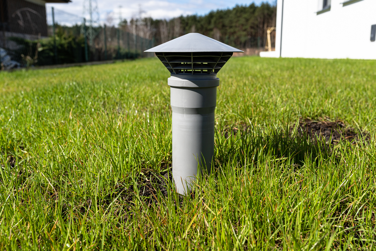 A septic tank vent pipe above the ground in a yard.