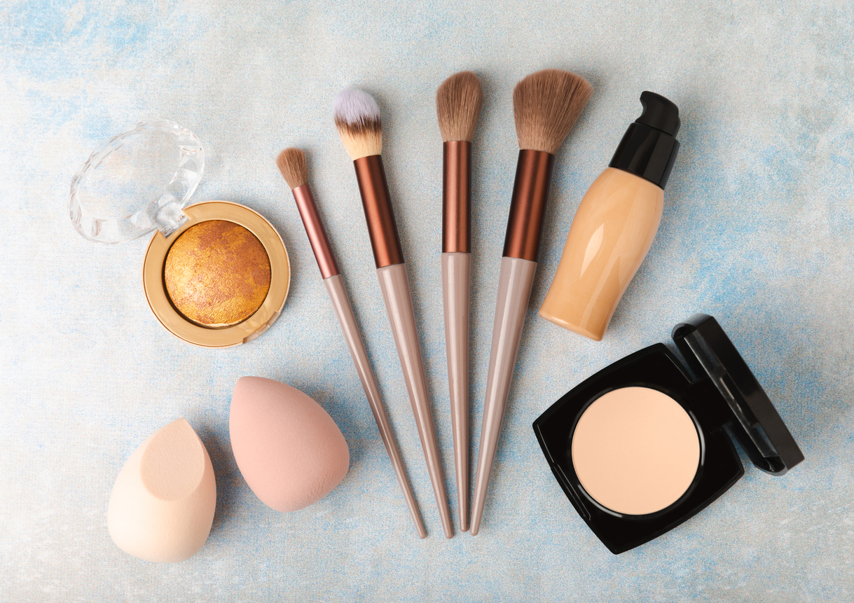 overhead view of makeup brushes, sponges, foundation and powder arranged on a table
