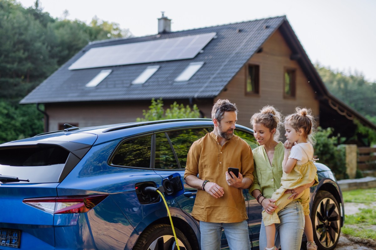 family standing in front of electric car with house in the background with solar panels