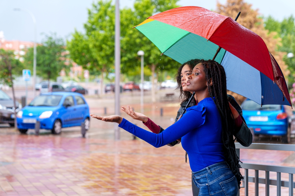 Two women under a colorful umbrella put their palms up outdoors to test whether it is raining.