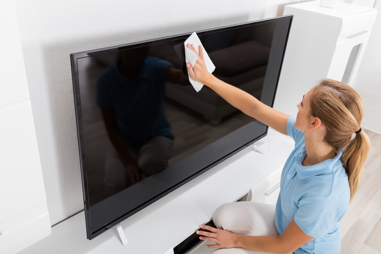 Young Smiling Woman Wiping Television Of Living Room At Home