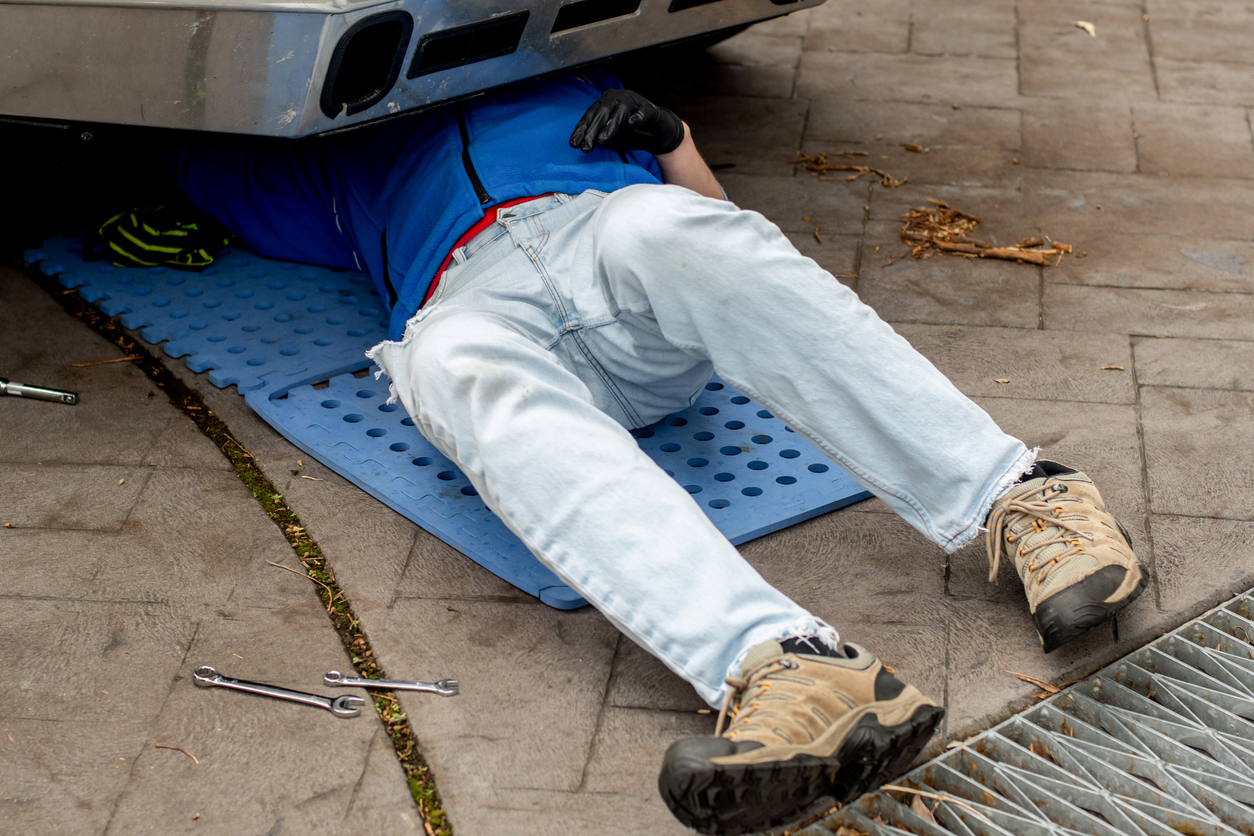 Man making repairs under car, lying on a cushioned mat