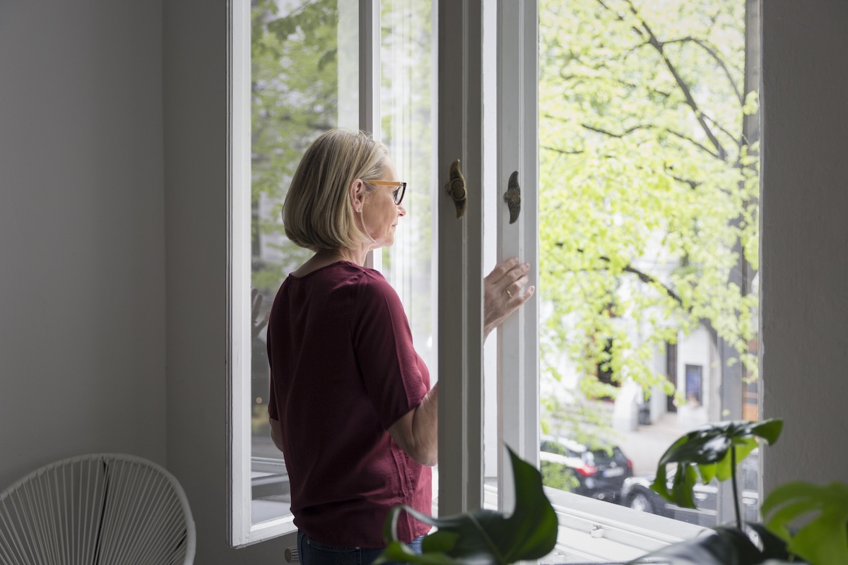 A woman wearing a red shirt opens a window.