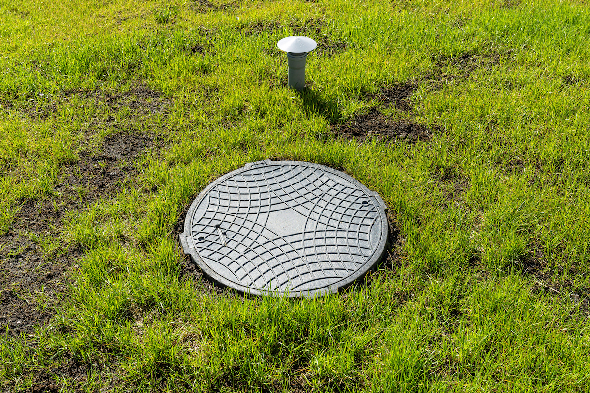Septic tank cover and vent from a household septic tank, surrounded by patchy grass.