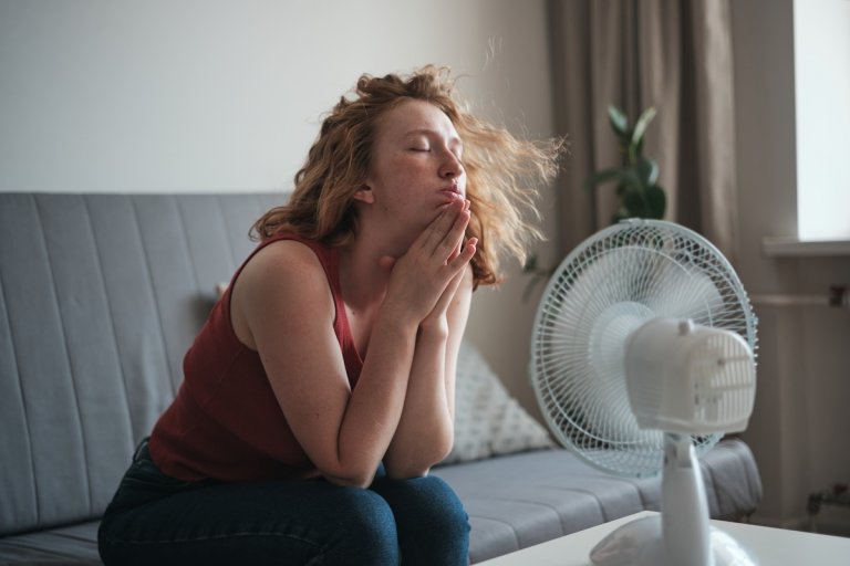 A woman sits in front of a fan to cool off in her humid home.