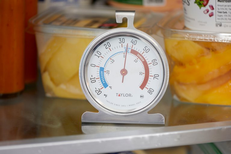 Close up of a refrigerator thermometer on a refrigerator shelf.