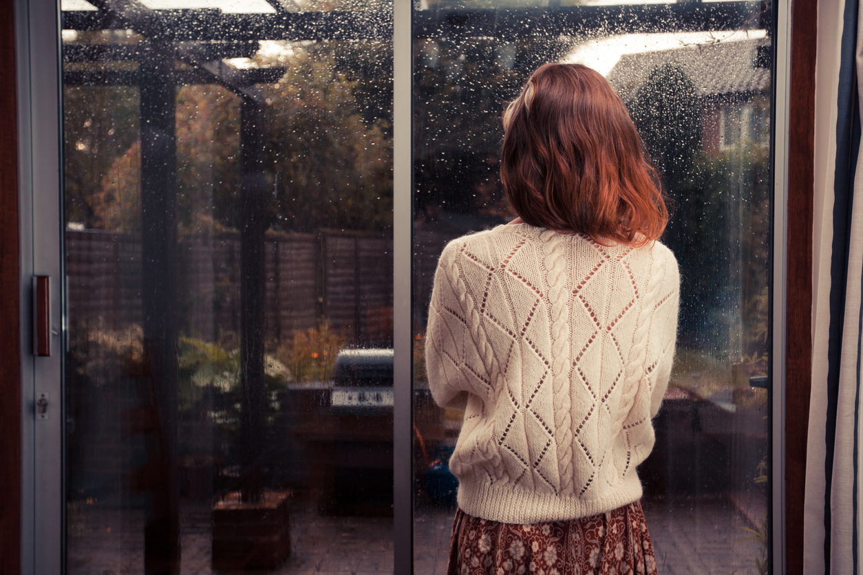 Young woman standing near a window watching rain outside