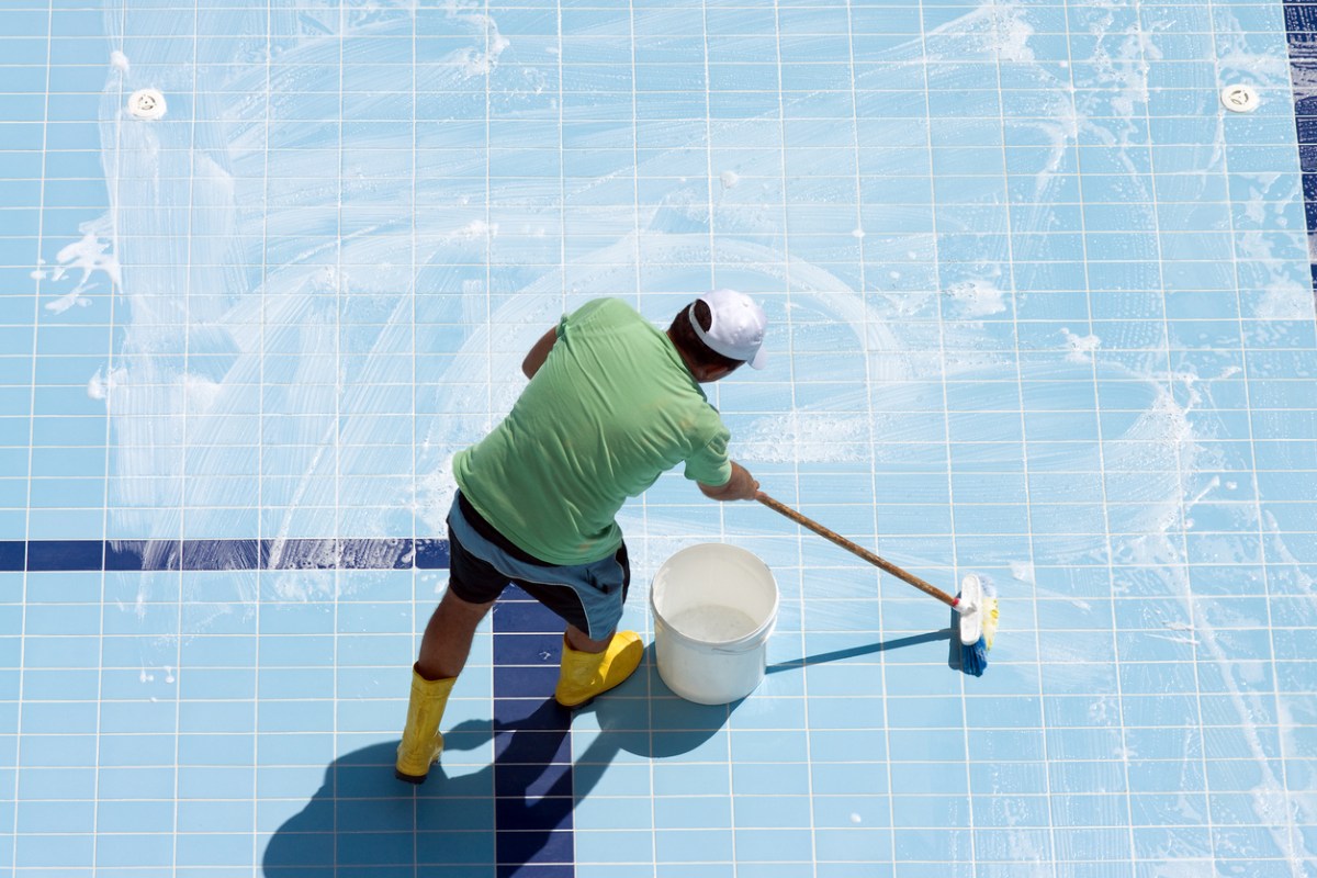 A person applying the best pool tile cleaner option to an empty pool using a large scrub brush