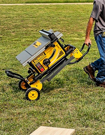 A person pulling the DeWalt 10-inch table saw through a yard using its rolling stand