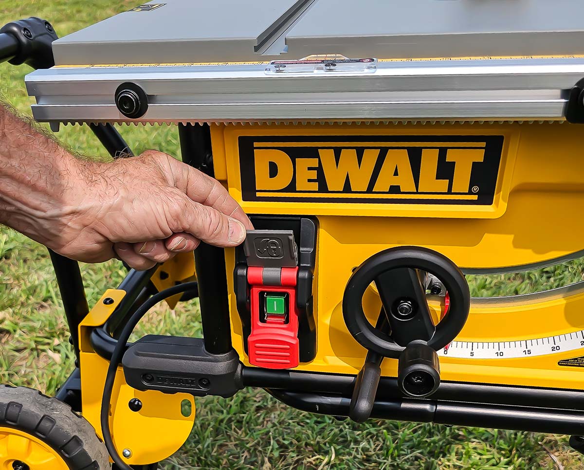 A person lifting a small door on the front of the DeWalt 10-inch table saw to reveal the tool's on/off switch