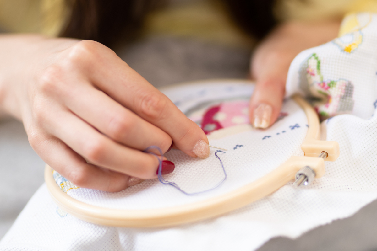 Closeup of a woman's hands embroidering art by hand on an embroidery hoop