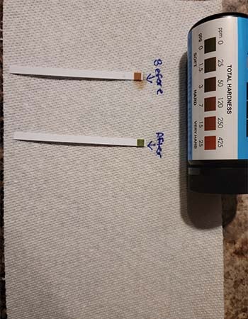 Two water testing strips showing the difference in water hardness before and after installing the Jolie shower head