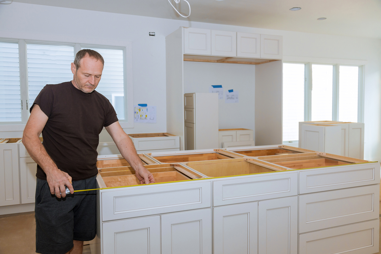 Man using measuring tape to measure the lower cabinets in a home kitchen for countertop installation