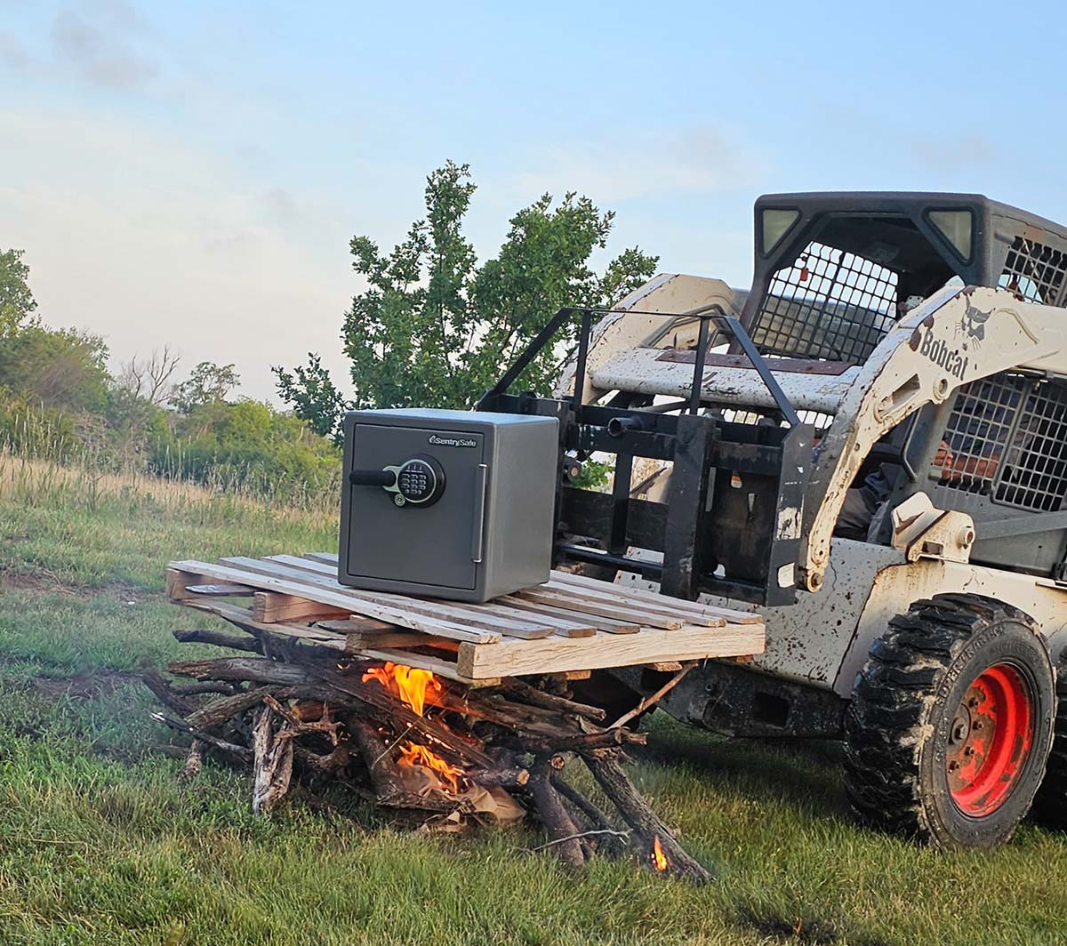The SentrySafe home safe sitting on a pallet held over a bonfire by a skid steer