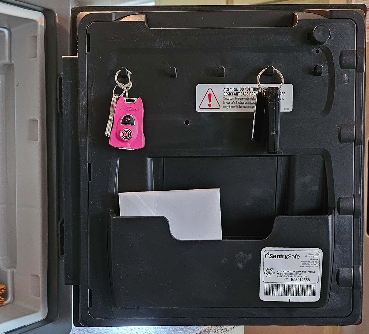 Inside the SentrySafe's door with two sets of keys hanging and a document in a pocket