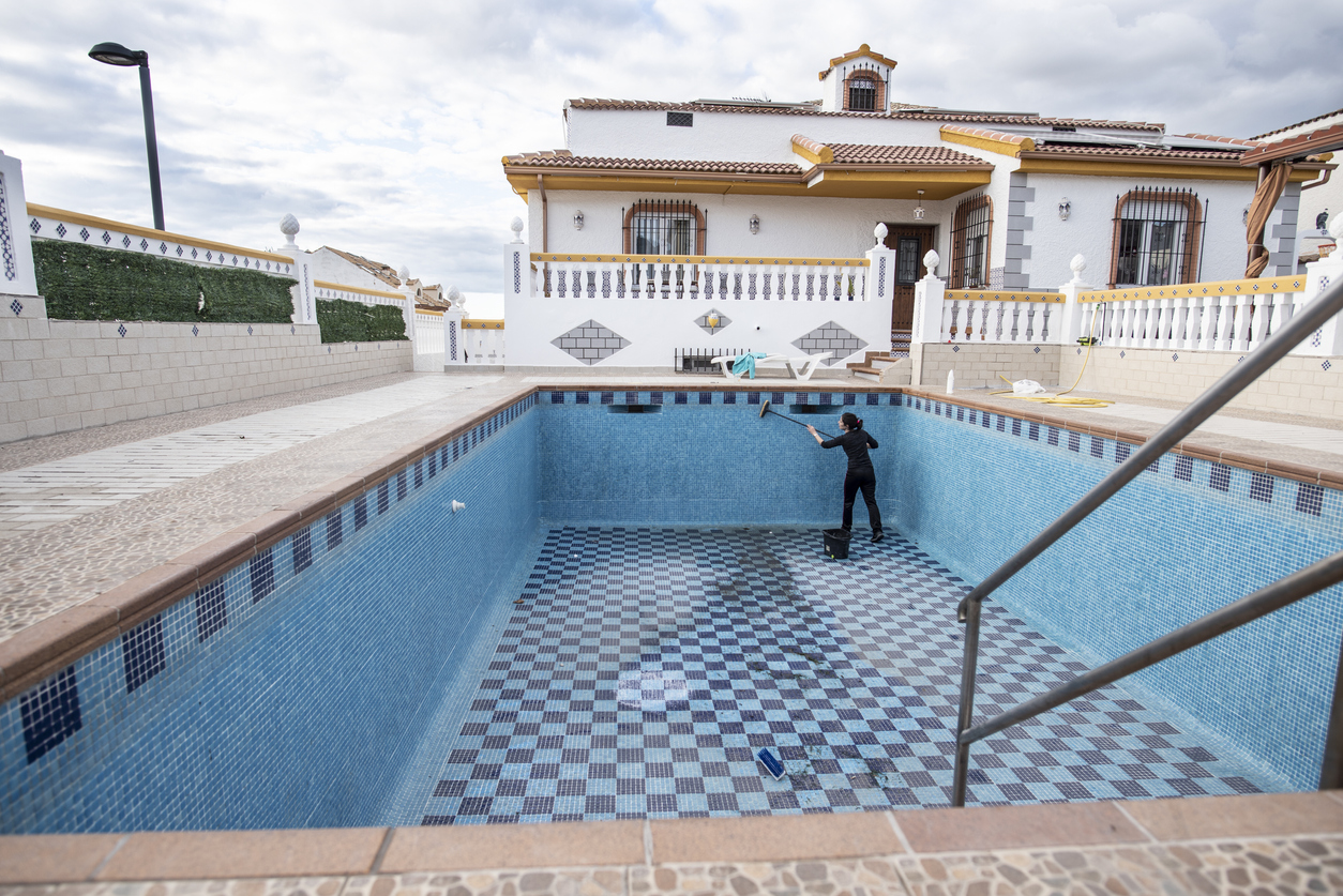 A person at the far end of a massive empty pool using the best pool tile cleaner option to clean the pool's tile walls