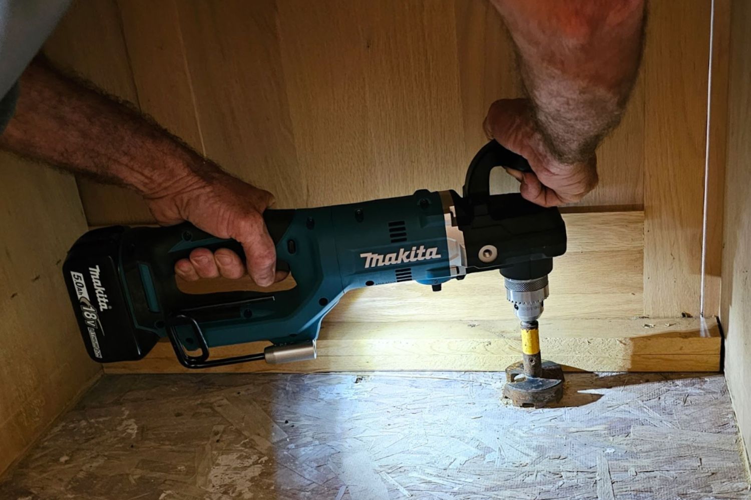 A person using the light on the Makita right-angle drill to work in a dark space