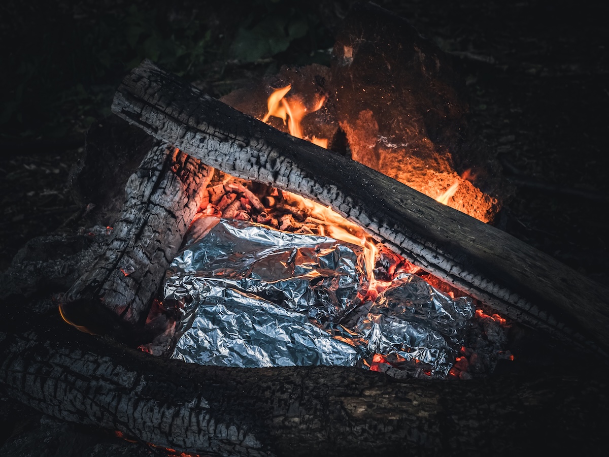 Tin foil packages of grilled food in a campfire.