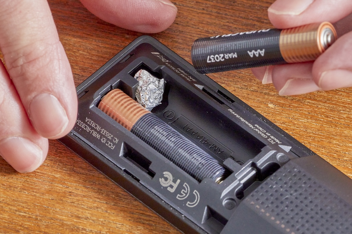 Person inserts AA battery in remote control, with small piece of aluminum foil covering one of the springs.