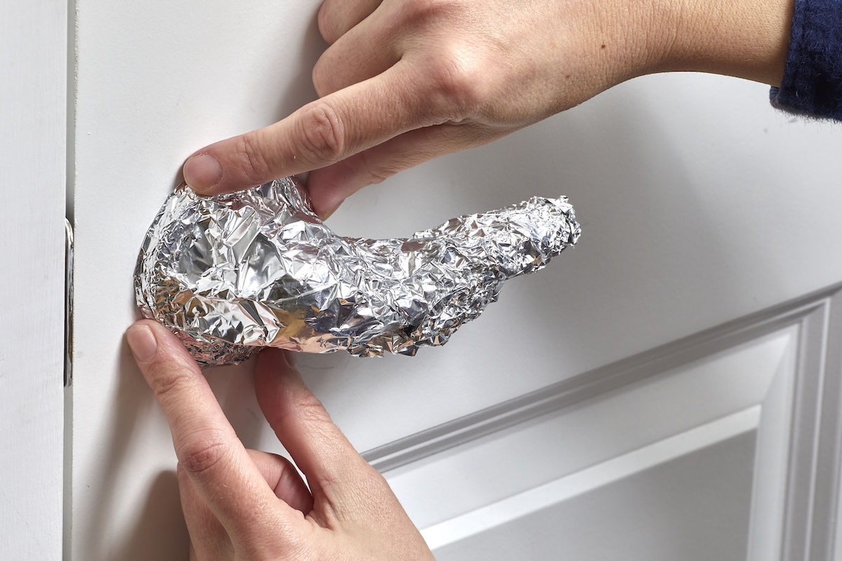 Woman secures aluminum foil over an interior door handle.