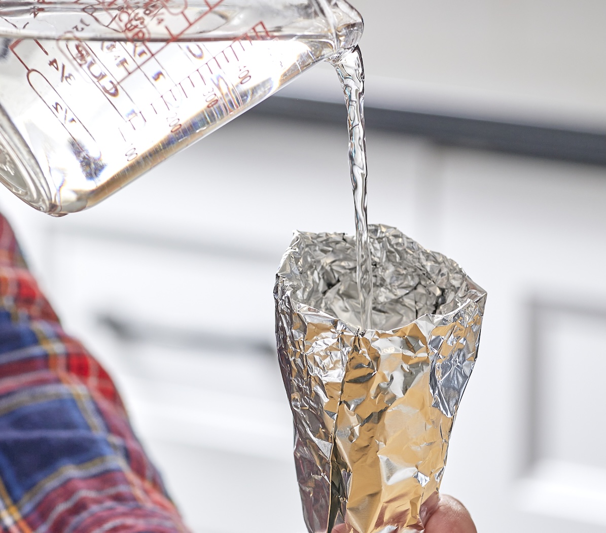 Person pours water from measuring cup into a funnel made of aluminum foil.