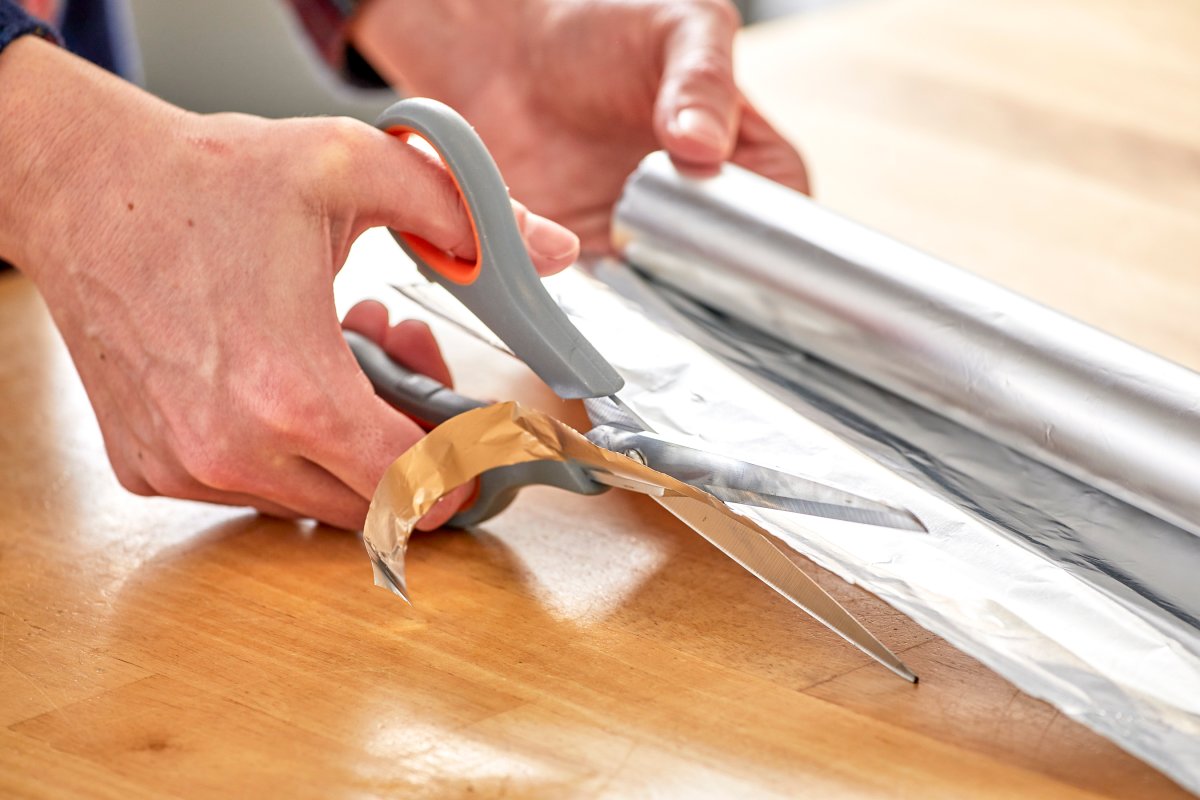 Woman cuts aluminum foil with scissors.