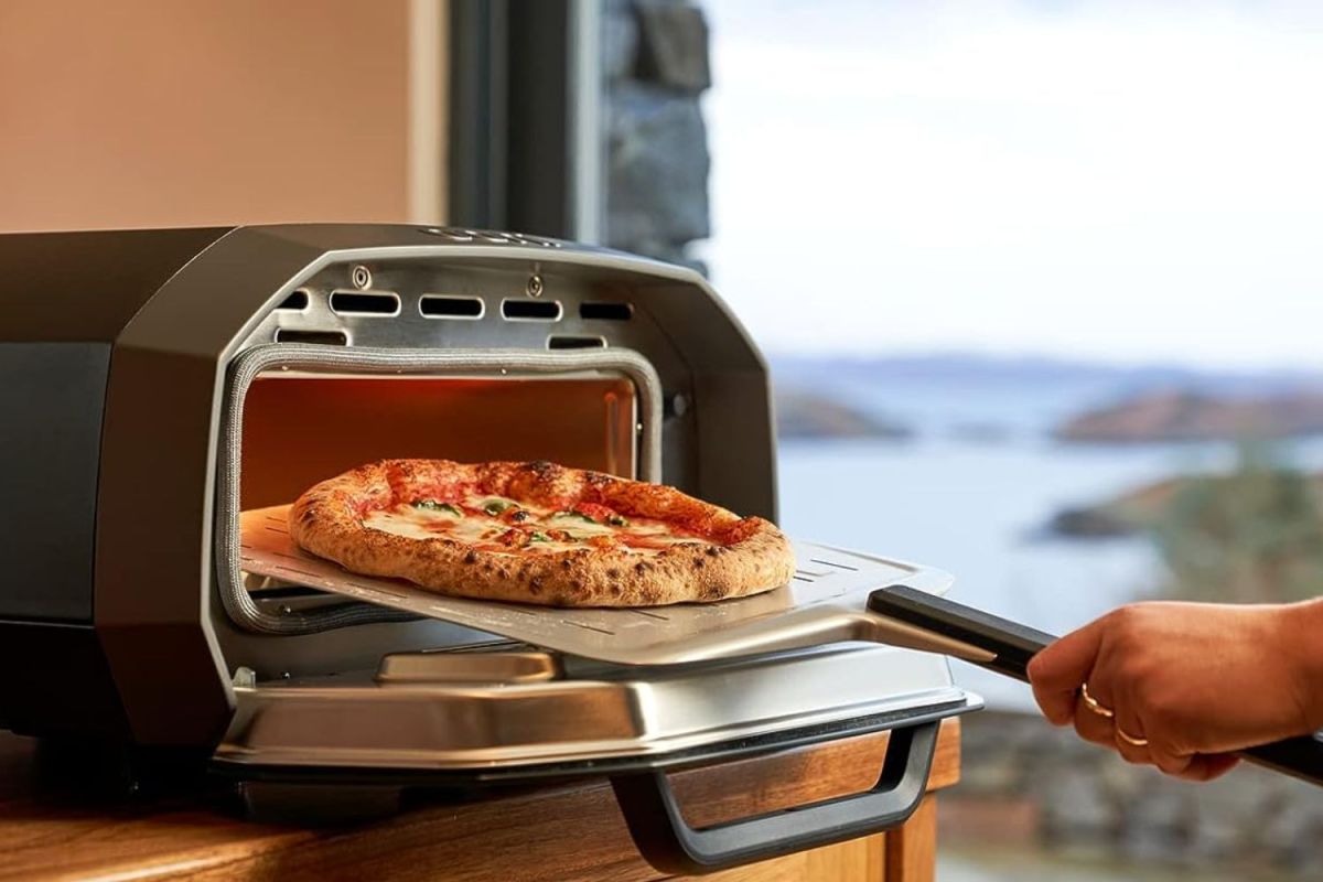A person pulling a delicious-looking pizza out of the best electric pizza oven