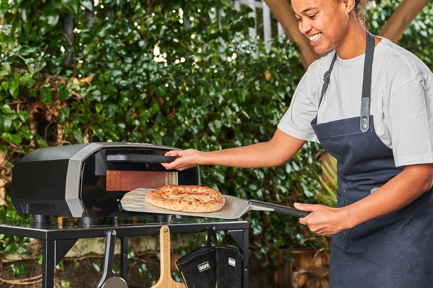 A person pulling a delicious-looking pizza out of the best electric pizza oven option that's set up outdoors