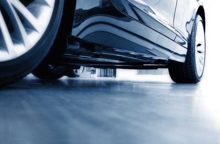 A side view of a shiny, modern blue car with silver rims on a grey garage floor.