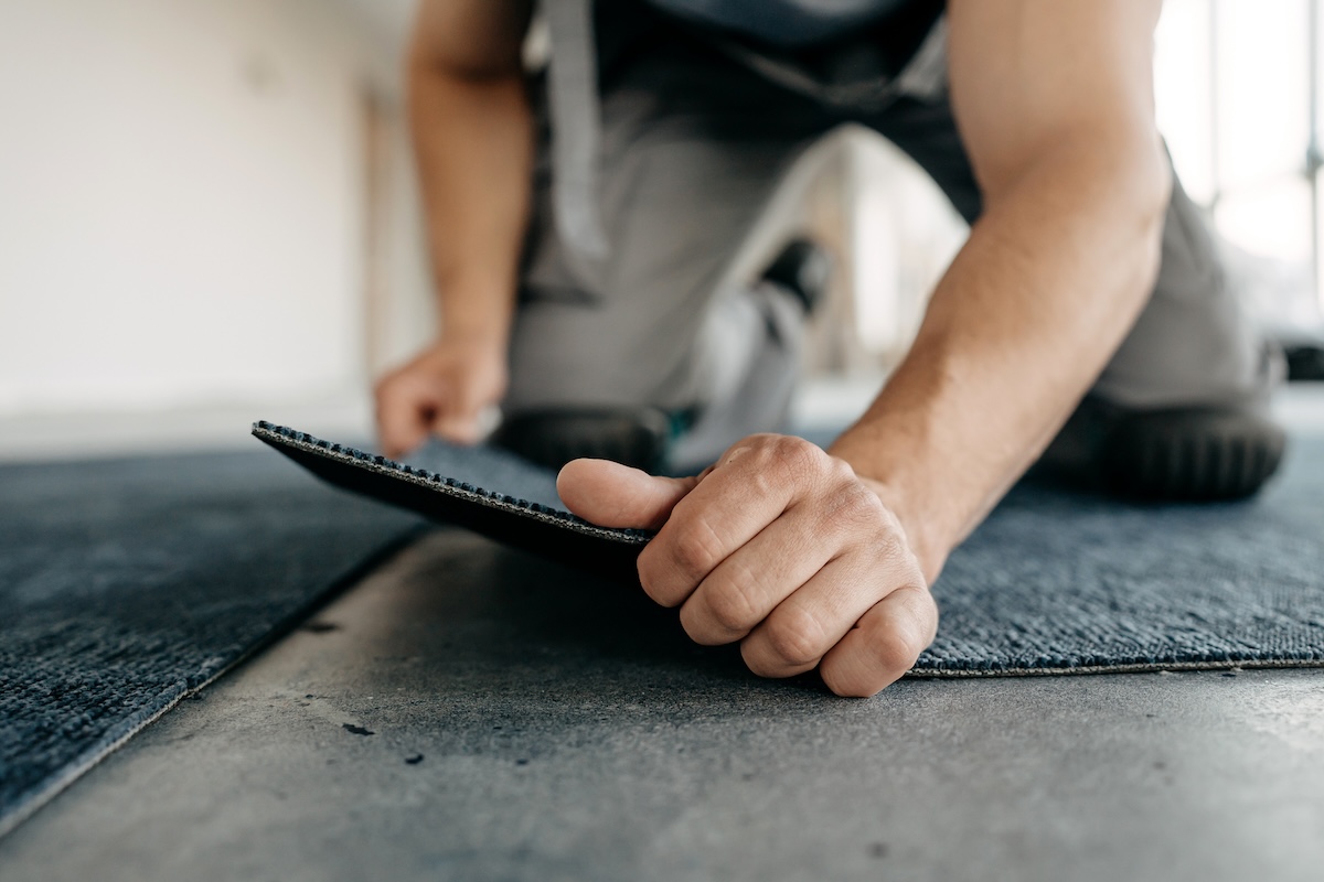 A carpenter installs carpet tiles.