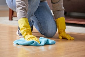 Woman wearing cleaning gloves uses microfiber cloth to clean hardwood floors.