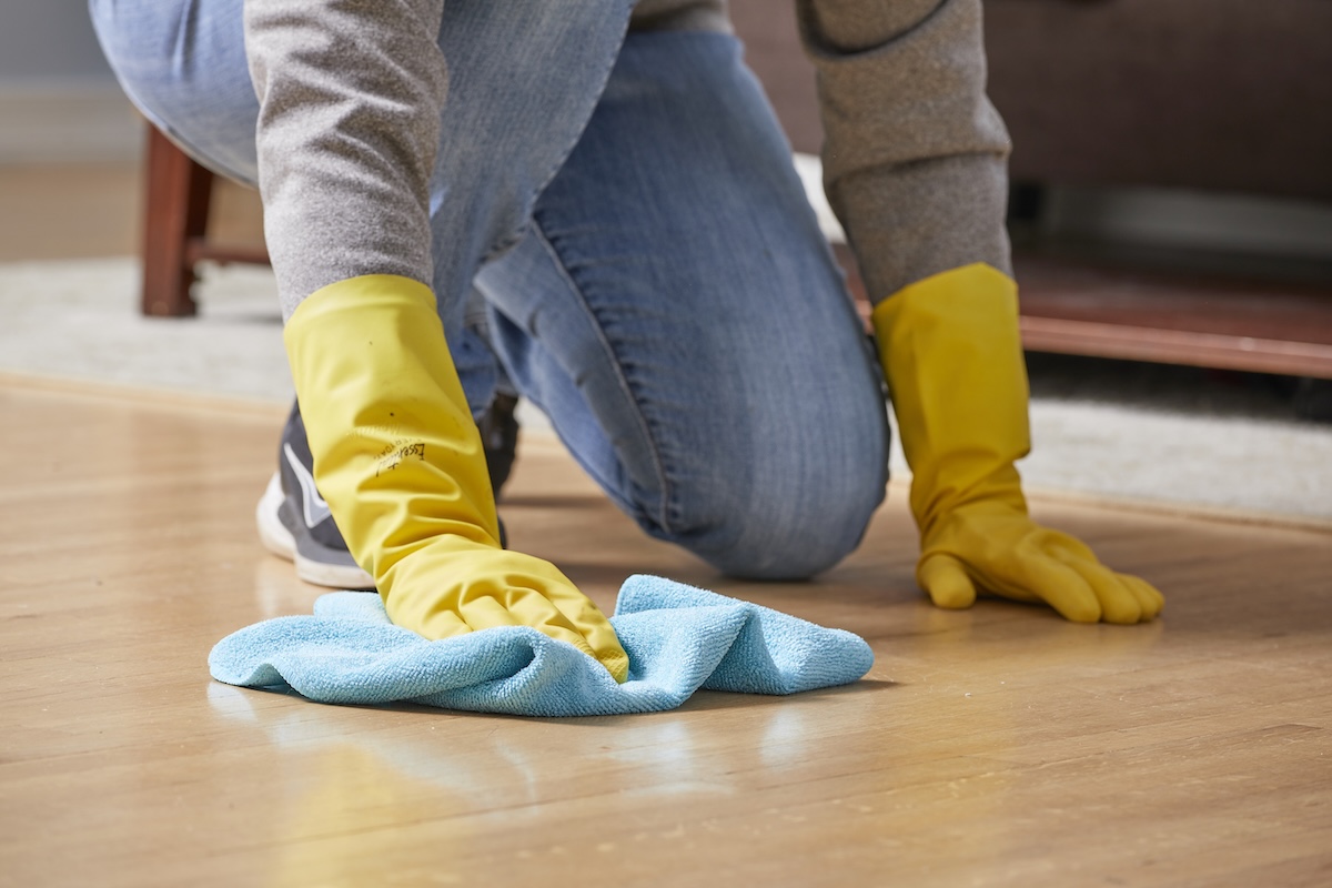 Woman wearing cleaning gloves uses microfiber cloth to clean hardwood floors.
