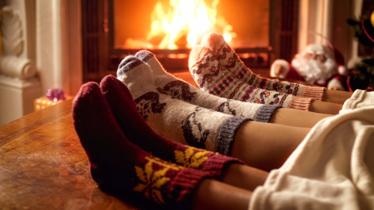 three pairs of feet with wool socks on table in front of roaring fireplace