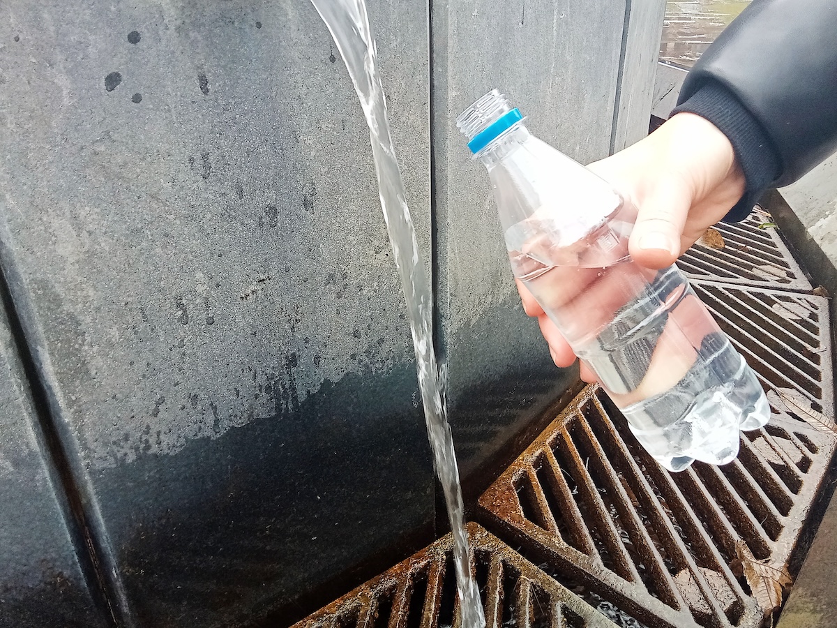 Someone fills up a plastic water bottle from a rain barrel.