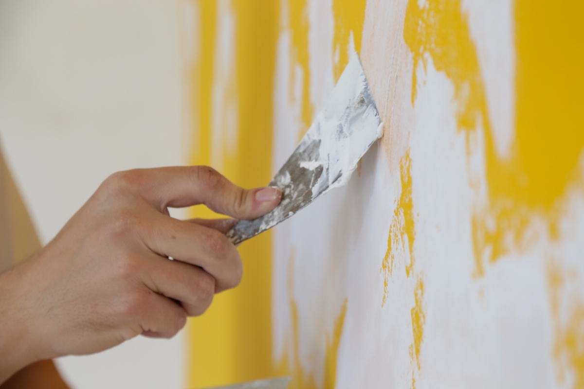 Person applying skim coat on yellow wall