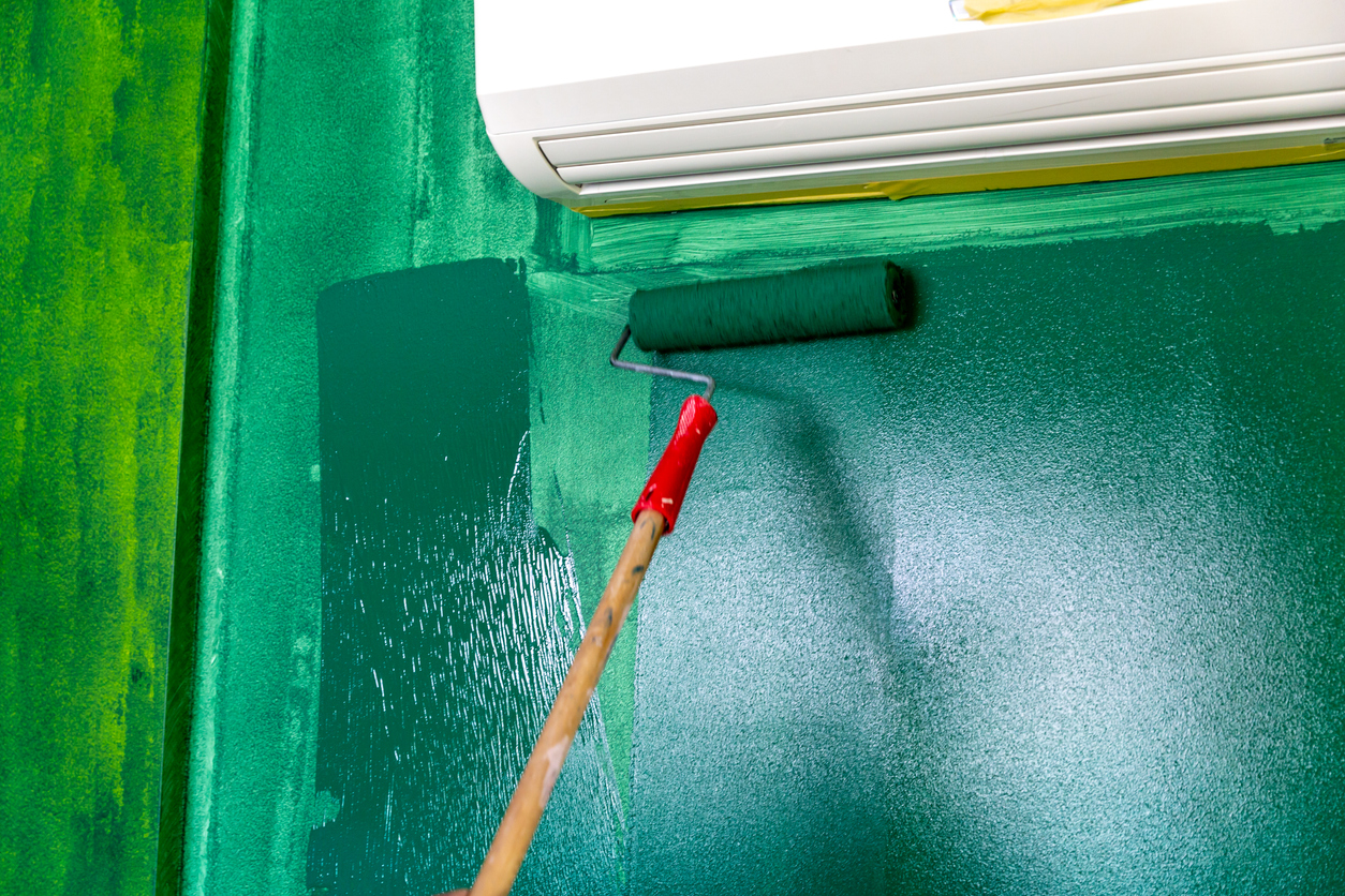 using roller to paint second coat of green paint onto wall