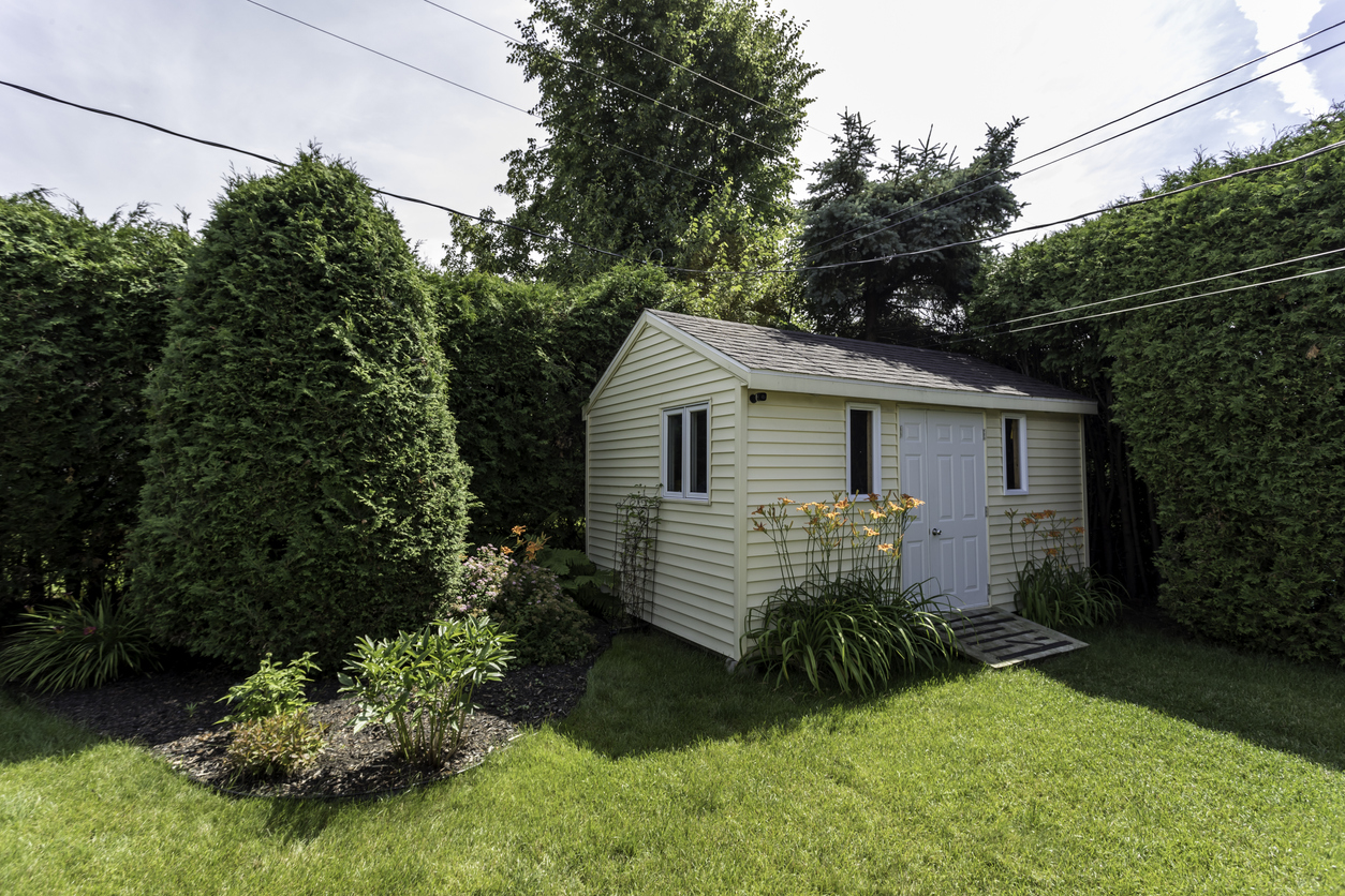 yellow-shed-in-a-green-yard-behind-shrubs-and-landscaping