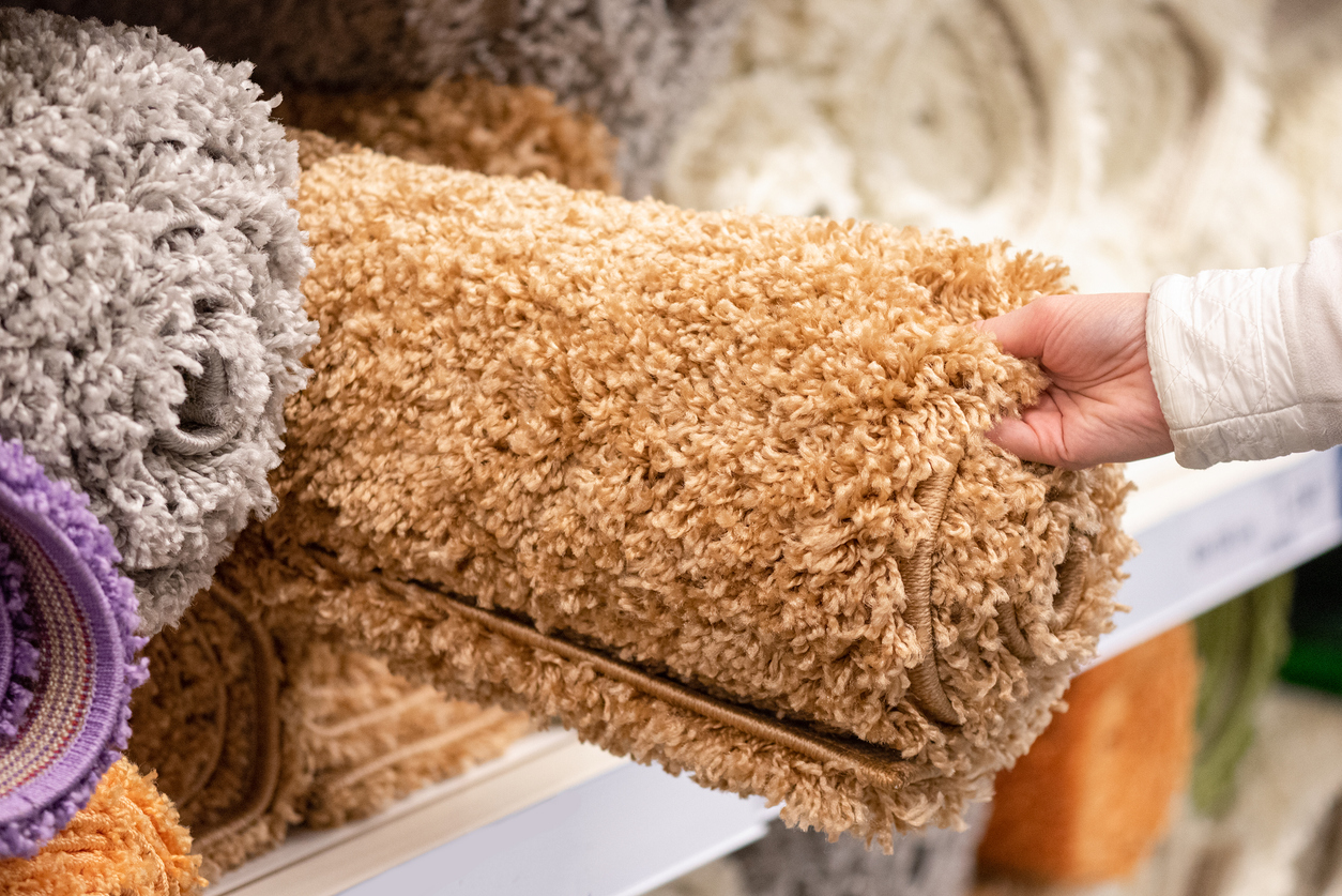 a-hand-holds-a-rolled-tan-carpet-remnant-from-a-shelf-of-other-remnants-and-rugs