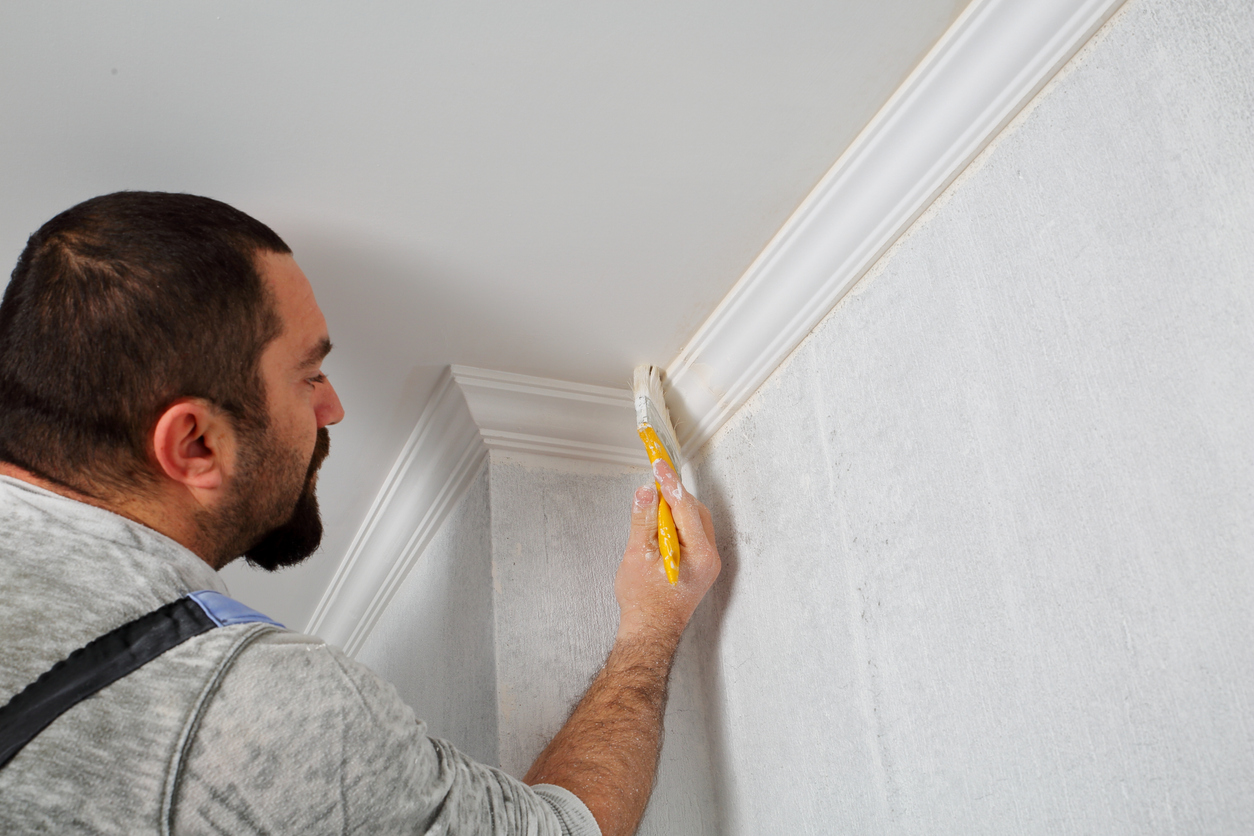 man painting the corner of a ceiling with crown molding trim